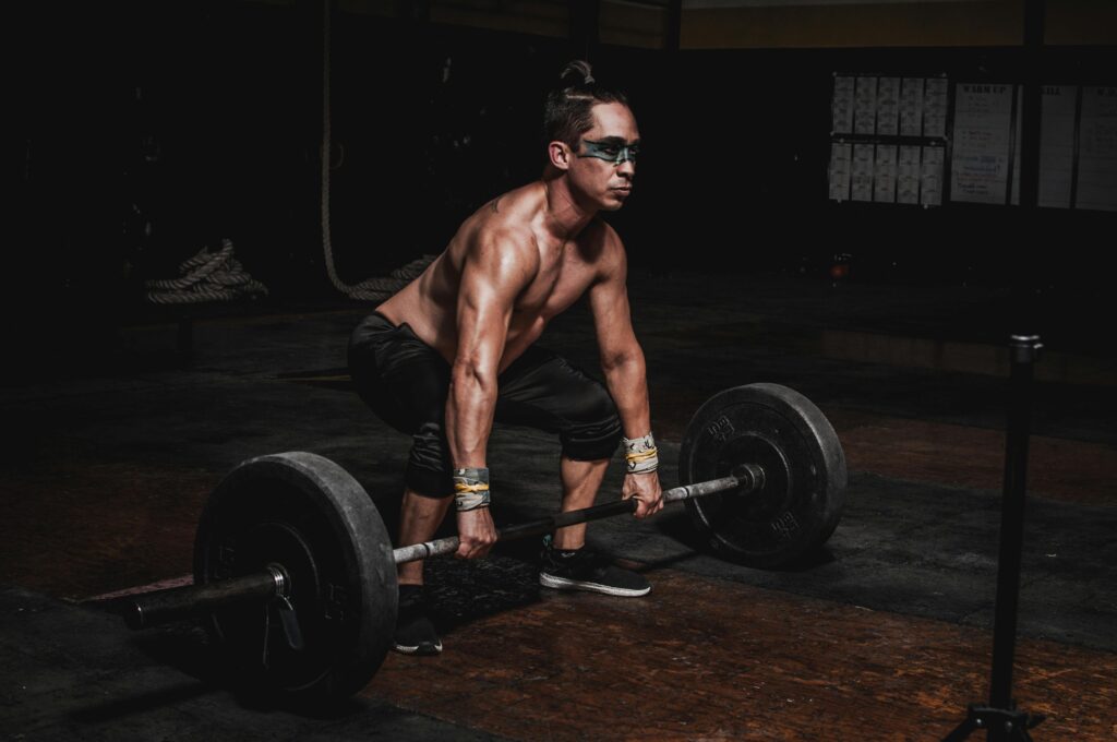 Homem realizando um levantamento terra com uma barra carregada de anilhas pesadas, exibindo concentração. Sua postura determinada reflete o esforço e a força necessários para completar o exercício com sucesso.