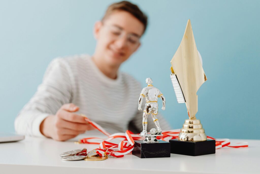 Homem sentado, segurando e admirando suas medalhas de vitória, com troféus ao lado, refletindo sobre suas conquistas alcançadas por meio de metas esportivas bem definidas.