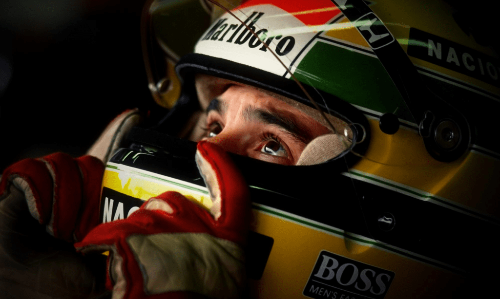 Ayrton Senna, usando seu capacete, olha para cima com expressão determinada, simbolizando a busca por inspiração e força interior para alcançar a alta performance no automobilismo.