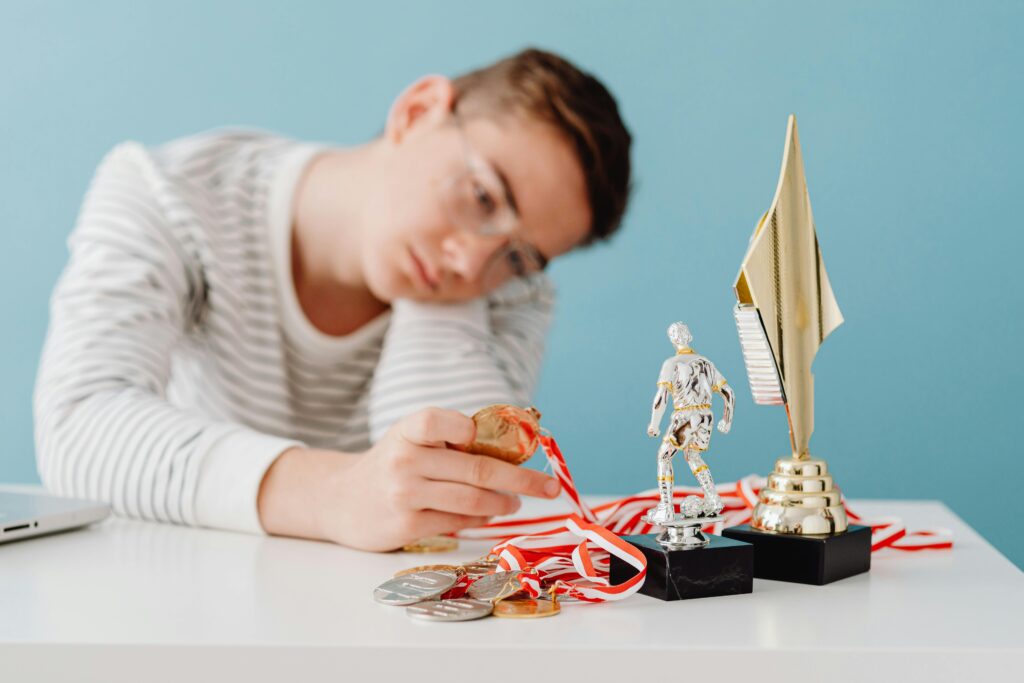 Atleta observando suas medalhas e troféus, cabisbaixo, refletindo sobre os desafios para recuperar seu alto desempenho no esporte.