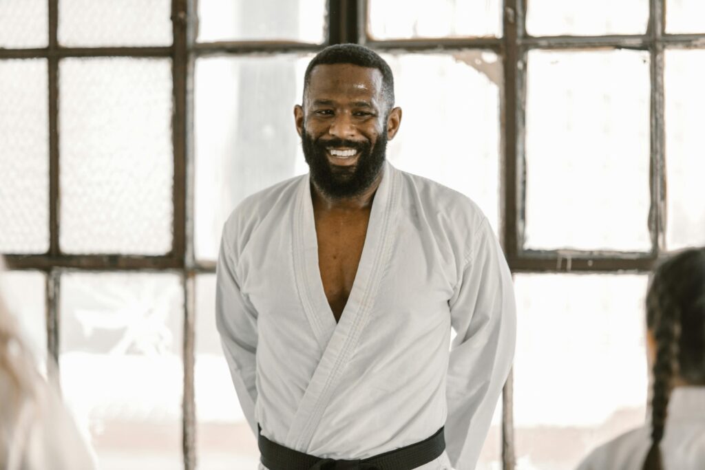 Um sensei faixa preta observa com satisfação seus alunos durante o treino, orgulhoso de ver sua confiança e autoeficácia se fortalecendo a cada movimento.