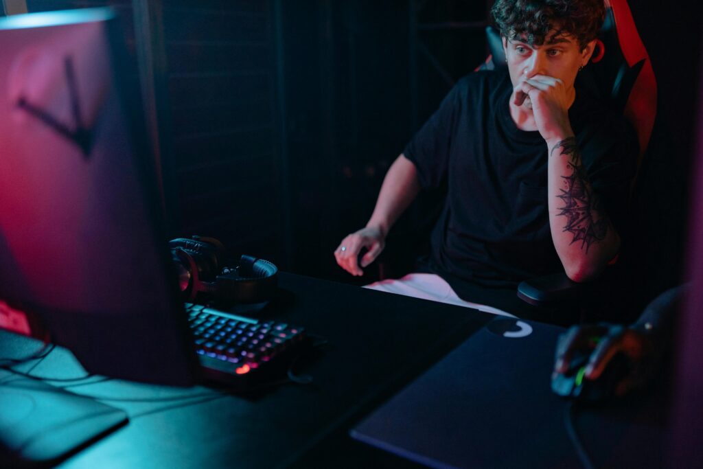 Atleta de eSports olhando para o PC, pensativo e ligeiramente abatido, refletindo sobre sua performance e buscando formas de superar seus desafios no competitivo.