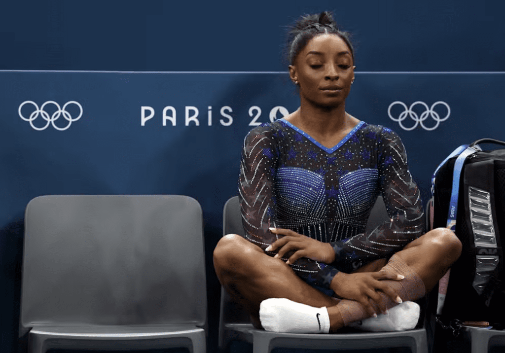 Simone Biles praticando mindfulness antes de sua competição nas Olimpíadas, sentada de pernas cruzadas em uma cadeira.