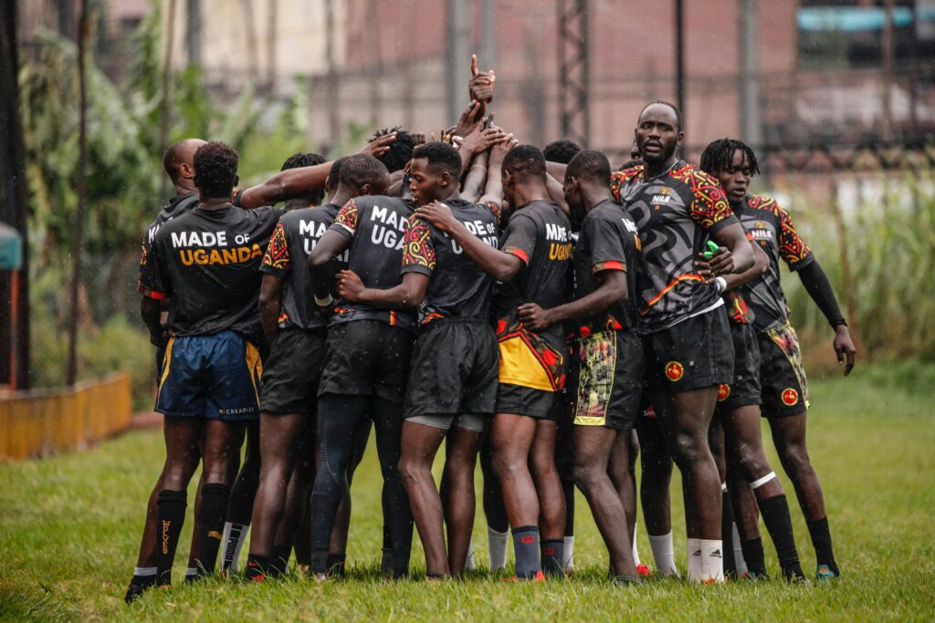 Time de Uganda se preparando  para uma partida de rugby, com os braços estendidos ao centro do círculo, simbolizando união.