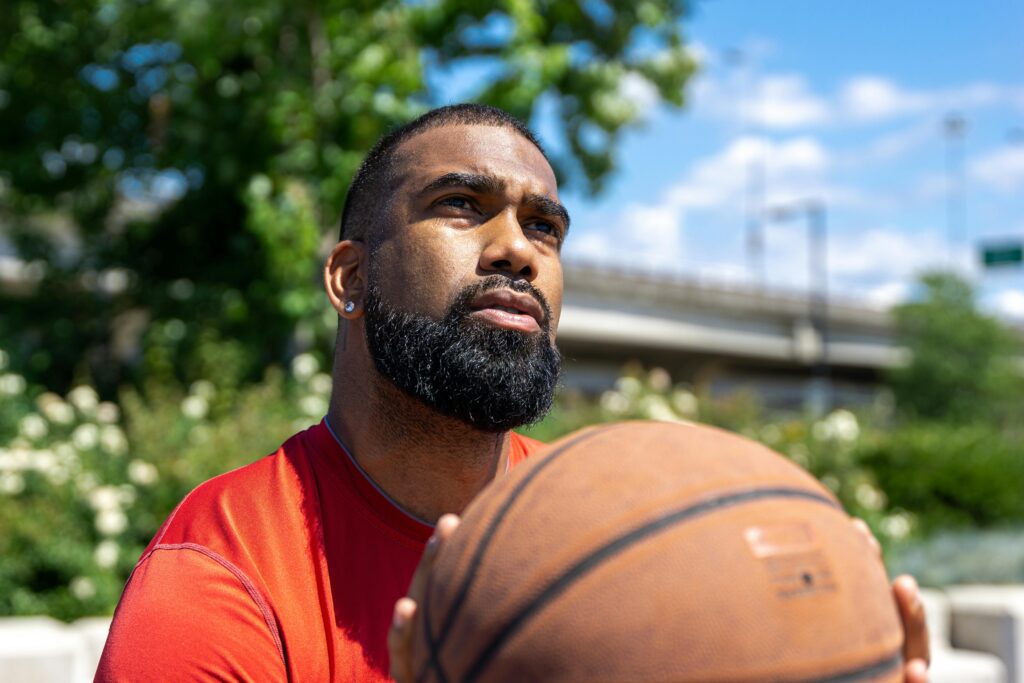 Homem segurando uma bola de basquete, analisando a força, direção e potência necessárias para fazer um arremesso preciso e acertar a cesta.