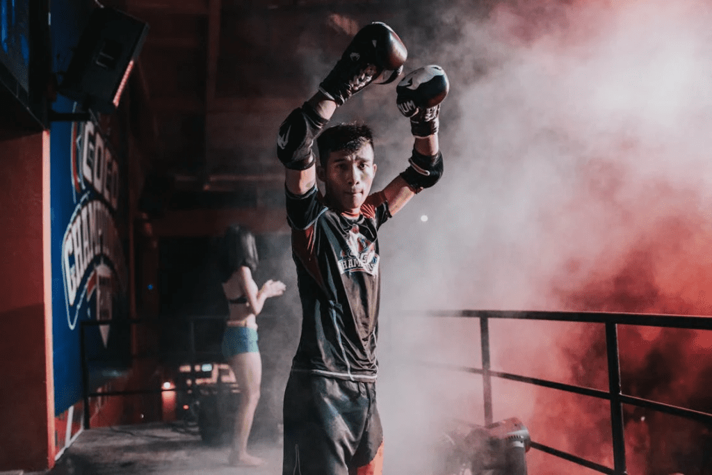 Um lutador no centro do palco, com os braços erguidos em comemoração, expressando a determinação e a força mental de um verdadeiro campeão. Seu olhar reflete foco absoluto e a emoção de conquistar a oportunidade de lutar por um título.