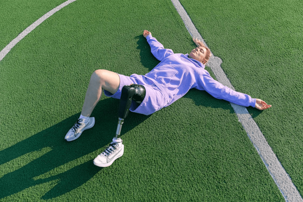 Uma mulher está deitada no gramado de um campo de futebol, de barriga para cima, recuperando-se do intenso treino. Com roupas esportivas e respiração profunda, ela aproveita o momento de descanso no centro do campo, sentindo o alívio após um dia de esforço e dedicação.