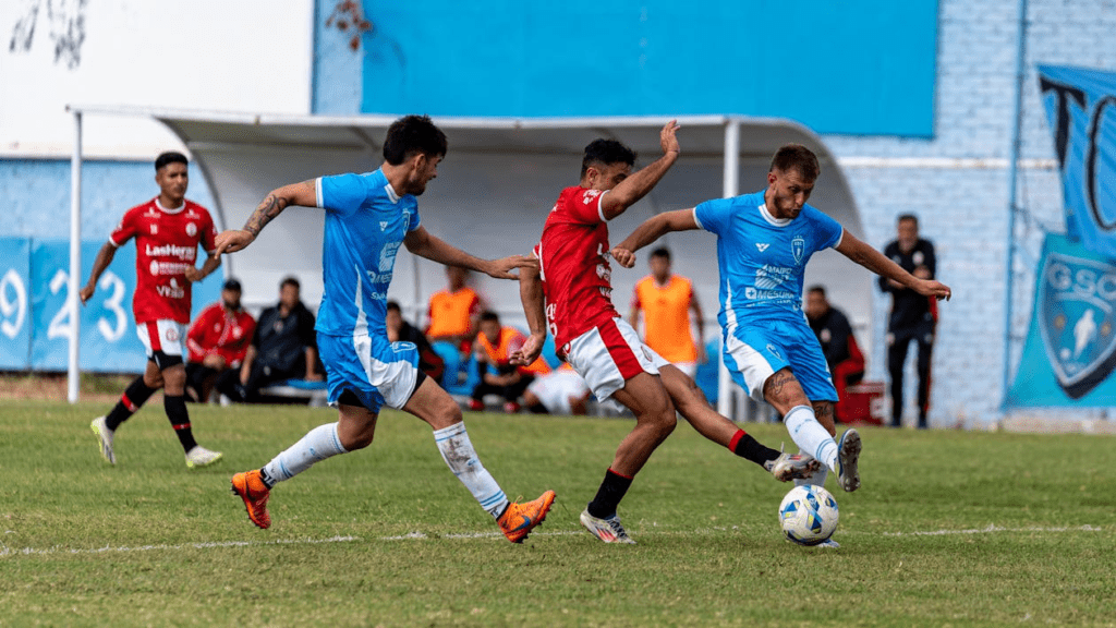 Jogador de futebol em uma jogada decisiva, cercado por dois marcadores, se preparando para finalizar ao gol. A cena destaca sua agilidade mental e física para tomar decisões rápidas sob pressão e buscar o melhor resultado para o time.