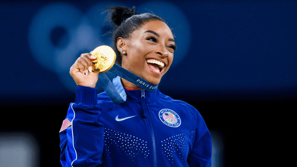 Simone Biles comemora a conquista da medalha de ouro nas Olimpíadas, simbolizando sua superação, foco na saúde mental e dedicação total à sua performance.