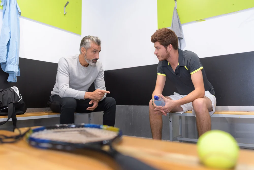 Psicólogo esportivo em sessão com atleta de tênis, oferecendo orientações estratégicas e apoio mental com a raquete sobre a mesa durante o atendimento personalizado.
