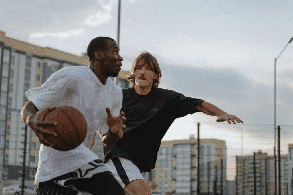 Dois jogadores de basquete de rua em momento decisivo próximo à cesta, disputando intensamente a jogada em uma quadra urbana. A imagem captura o confronto direto e a tensão de uma tomada de decisão crítica, típica do streetball, com energia, habilidade e competitividade em destaque.