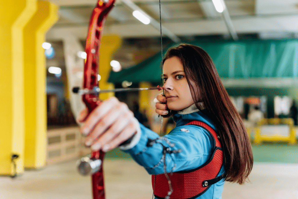 Atleta de arco e flecha concentrada, em total foco e controle emocional, aguardando o momento exato para soltar a flecha e acertar o alvo com precisão. A imagem transmite tomada de decisão, disciplina mental e performance no esporte de tiro com arco.