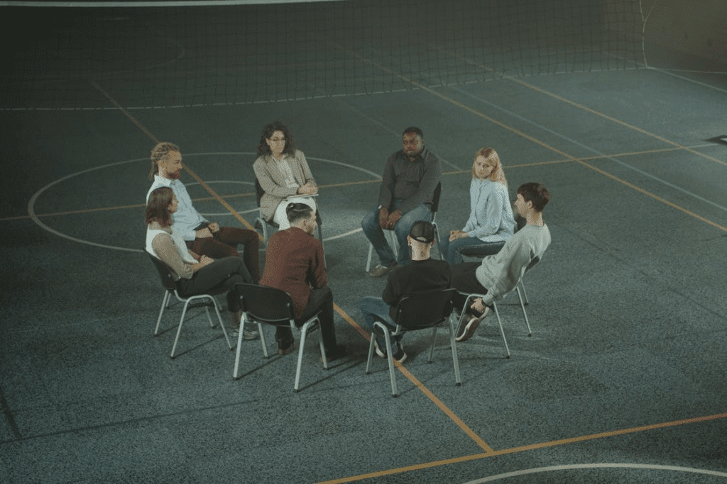 Roda de cadeiras posicionada dentro de uma quadra de vôlei, próxima à rede, simulando uma sessão coletiva de orientação, reflexão ou treinamento em grupo.