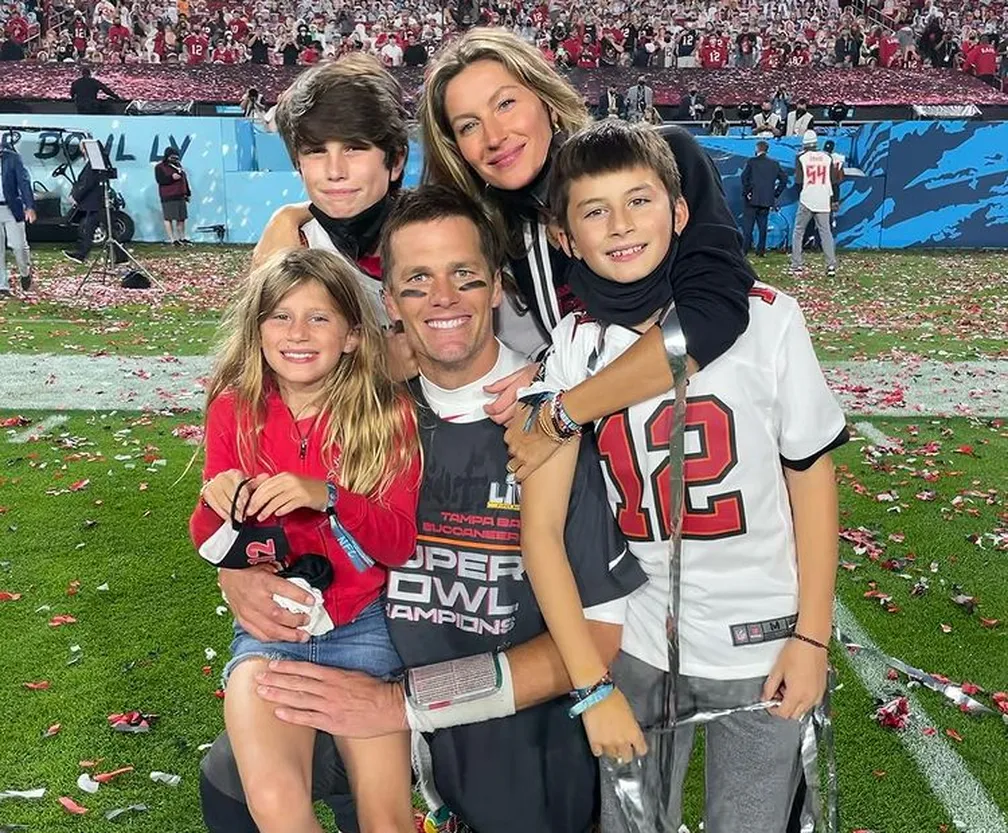 Tom Brady comemora o título da NFL com o Tampa Bay Buccaneers ao lado da família, em campo, com a torcida ao fundo celebrando a conquista do Super Bowl.