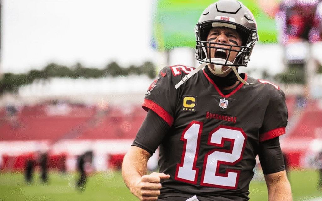 Tom Brady vibrando intensamente após uma jogada de sucesso com a camisa do Tampa Bay Buccaneers, comemorando dentro de campo com entusiasmo.