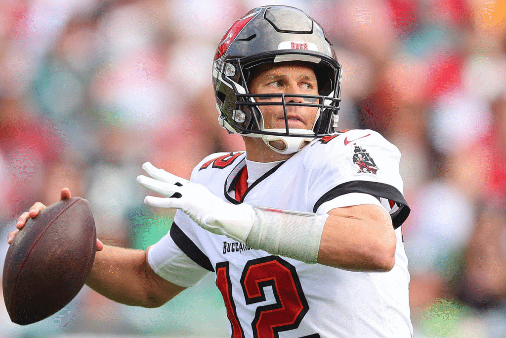 Tom Brady concentrado, preparando-se para lançar a bola em uma jogada pelo Tampa Bay Buccaneers, com o braço em posição de arco e expressão de foco total.