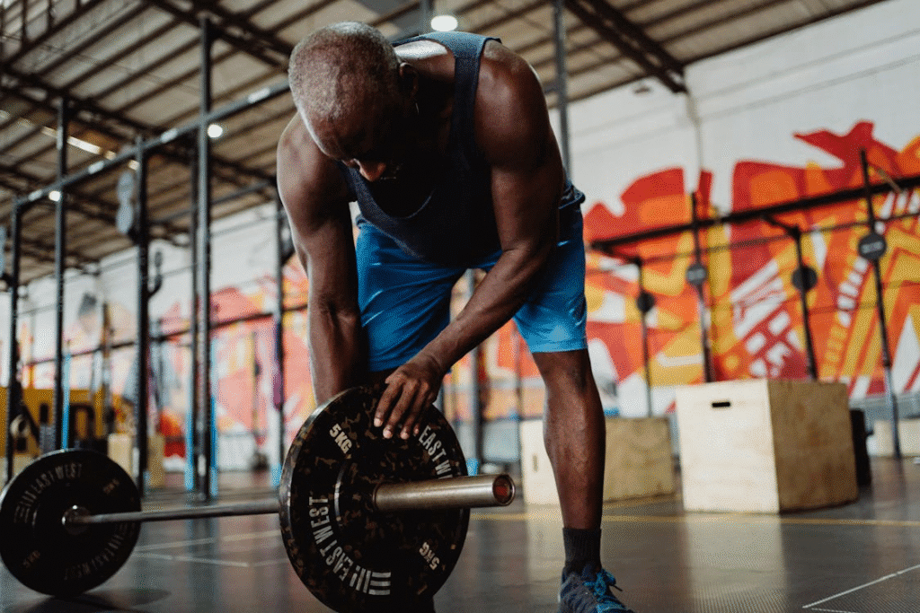 Atleta de alta performance preparando-se para treino de força, posicionando anilhas de 10kg em uma barra no solo como parte da rotina de musculação e condicionamento físico.