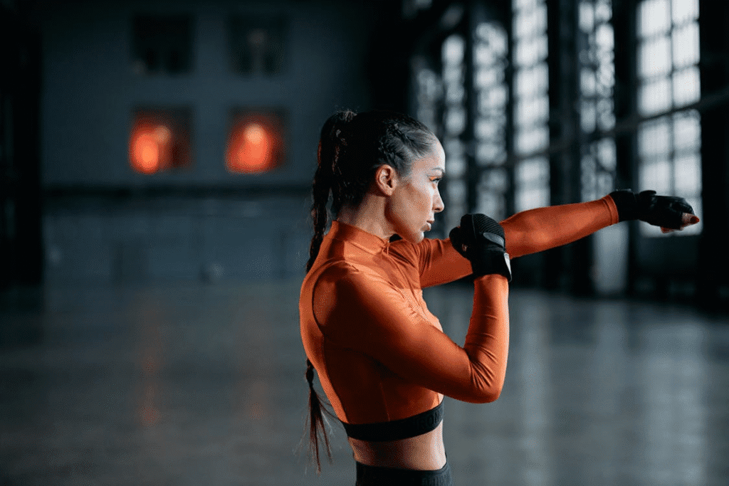 Lutadora em treinamento dentro de uma arena, com o braço estendido em posição de combate, se preparando mental e fisicamente para uma competição futura.