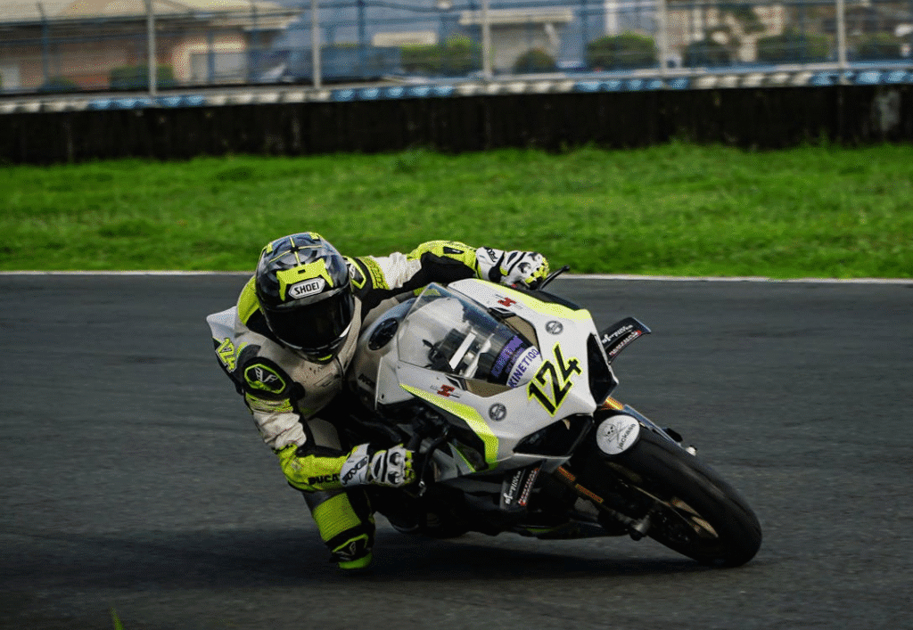 Piloto de motovelocidade realizando curva em alta velocidade, totalmente concentrado, usando uniforme e equipamentos de proteção em uma competição profissional.
