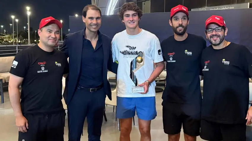 João Fonseca ao lado de sua equipe e de Rafael Nadal, segurando o troféu e celebrando o trabalho conjunto. A foto destaca a importância do apoio técnico e psicológico no desenvolvimento contínuo do atleta.