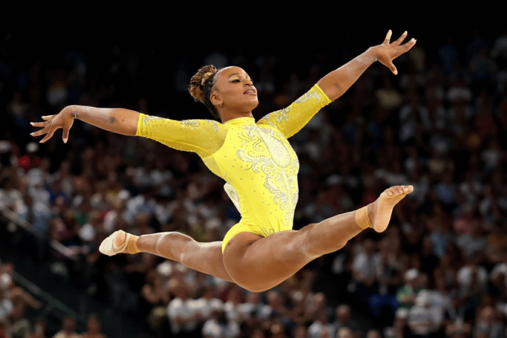 Rebeca Andrade em plena apresentação olímpica, executando um salto com braços e pernas completamente esticados, demonstrando técnica e força na ginástica artística.