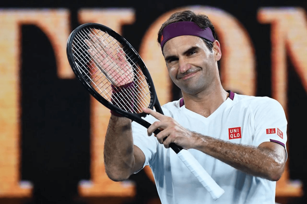 Roger Federer celebra e agradece ao público usando a raquete como palma para bater palmas após uma vitória. A imagem transmite elegância, respeito e conexão emocional com os fãs, reforçando o espírito esportivo e a mentalidade vencedora do suíço. Ideal para artigos sobre fair play, mentalidade de campeão e legado no tênis.