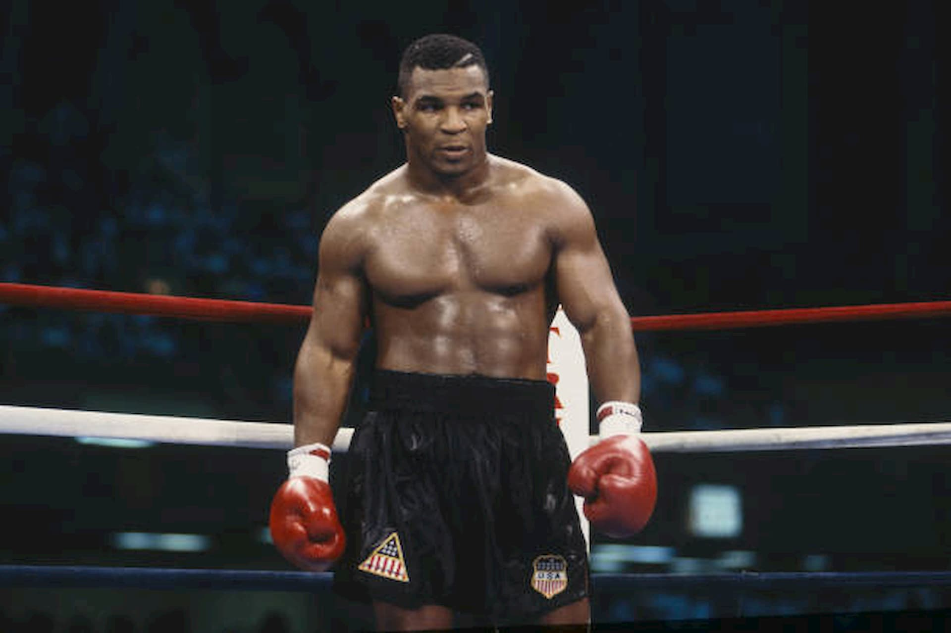 Mike Tyson em pé dentro do ringue, totalmente uniformizado e em estado de concentração máxima antes do início da luta. A imagem representa preparação mental, presença, foco absoluto e controle emocional momentos antes da competição, elementos-chave da alta performance no boxe e no esporte em geral.